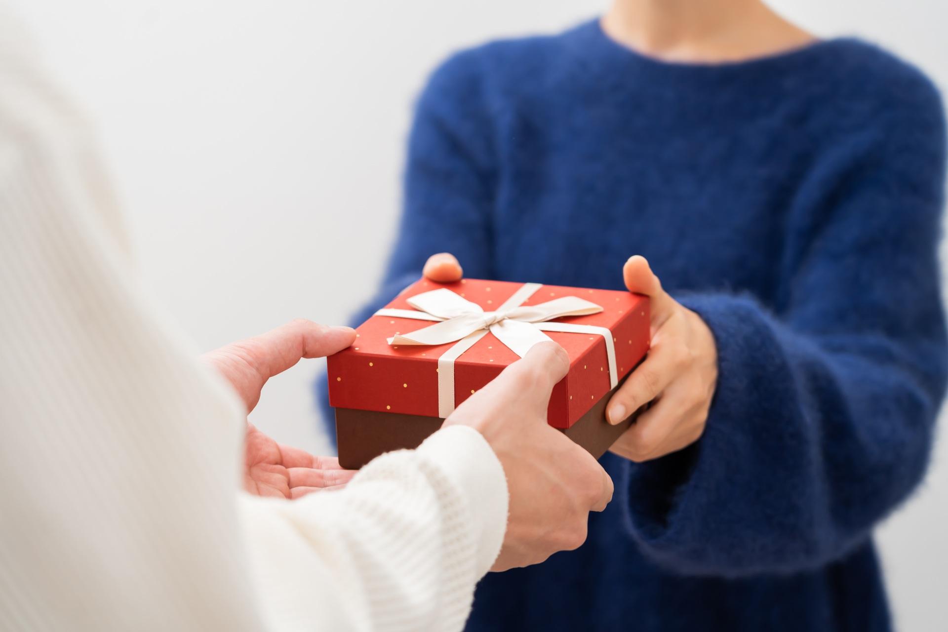 Zwei Personen beim Überreichen eines roten Geschenks | Geschenkkorb Weihnachten